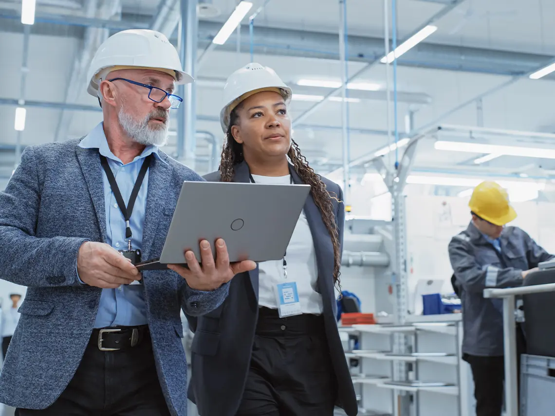 Two managers wearing hardhats while touring a manufacturing facility.