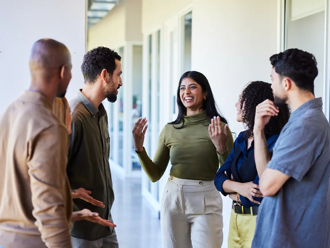 A group of 5 people talking in the hallway of an office building.