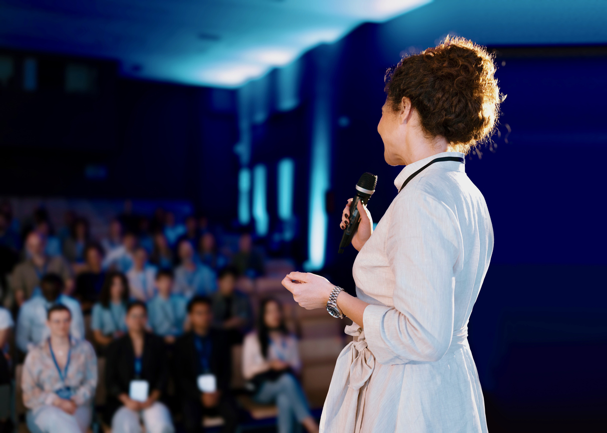 Inspired professional woman presenting a speech in a large conference setting.