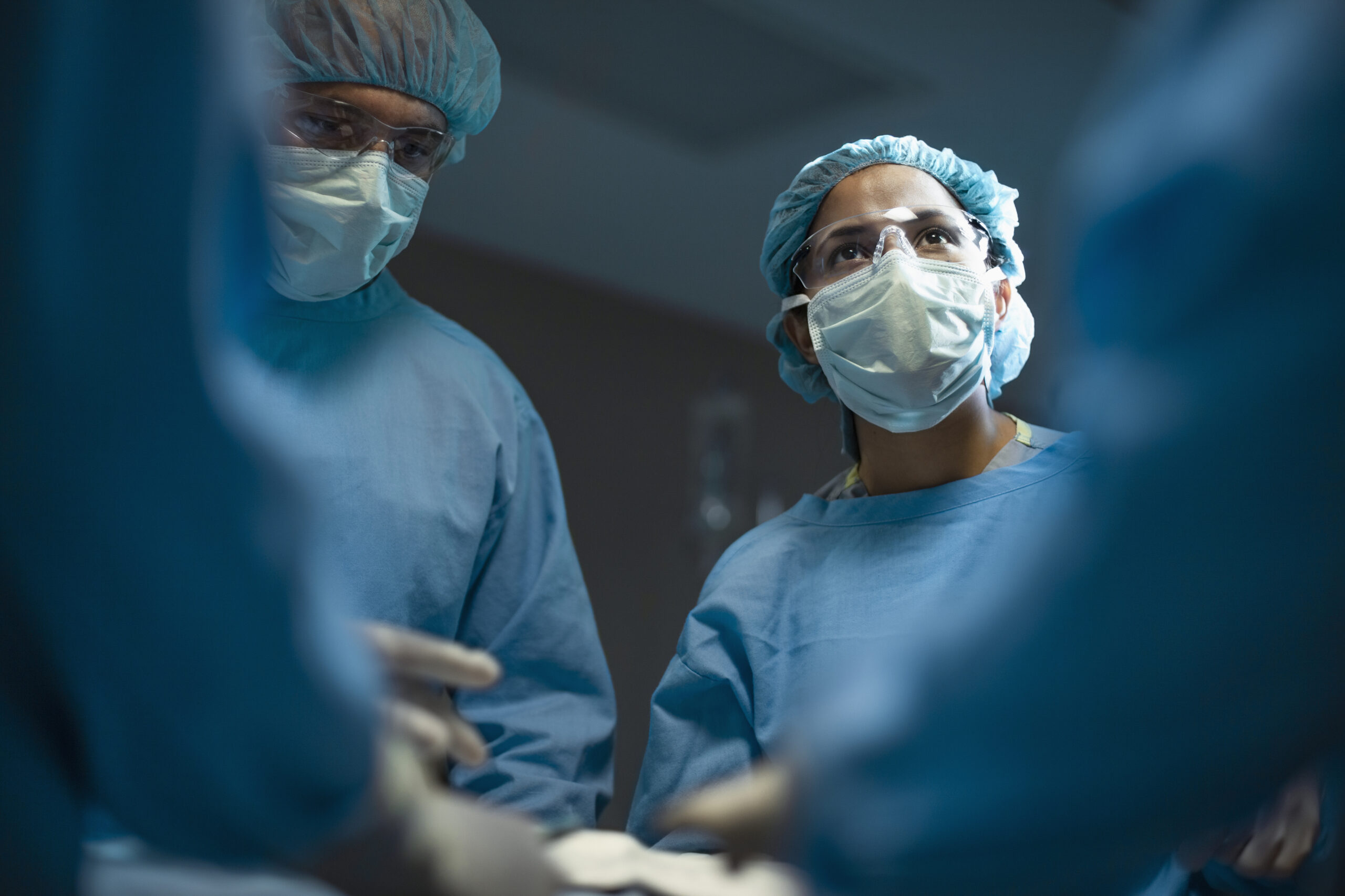Hispanic medical professional doctor nurse looking upward during surgery operation procedure in hospital with colleagues